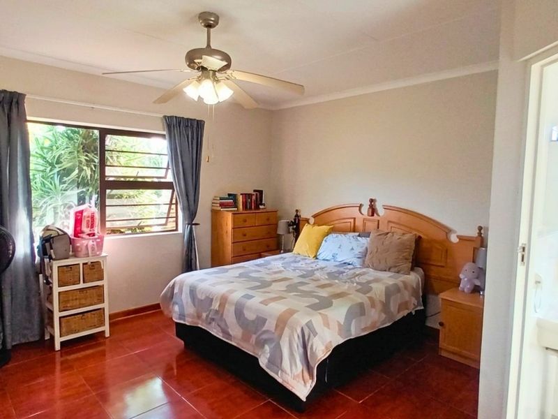 A bedroom featuring tiled flooring, a ceiling fan, and an adjoining en-suite bathroom area.