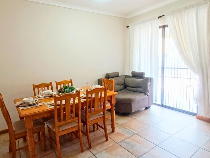 A dining area featuring ceramic floor tiles and a sliding glass door with security gate, providing access to the outdoor space.