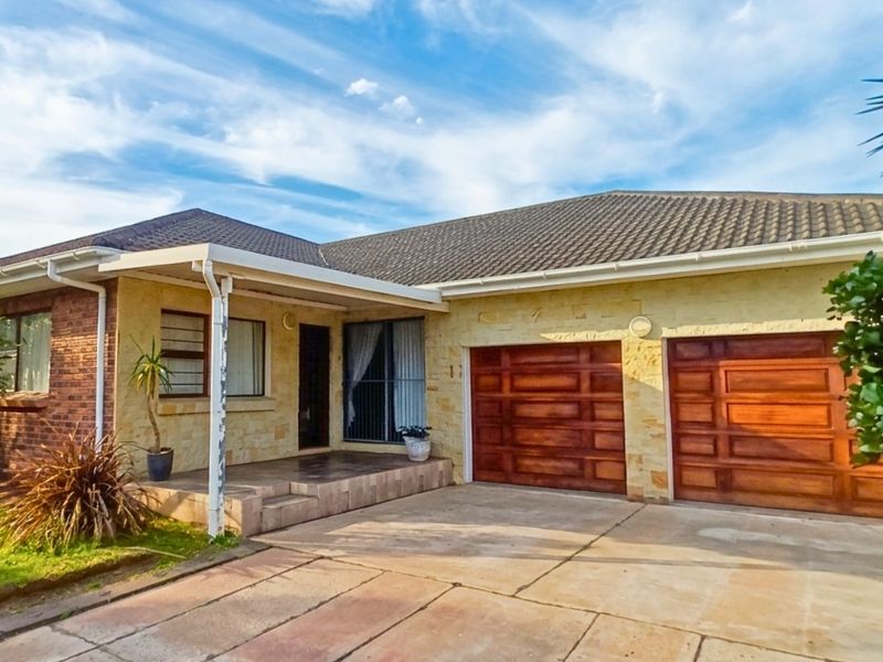A single-story residential home featuring a tiled roof, stone-clad facade, covered entrance porch, and a double garage with wooden doors.