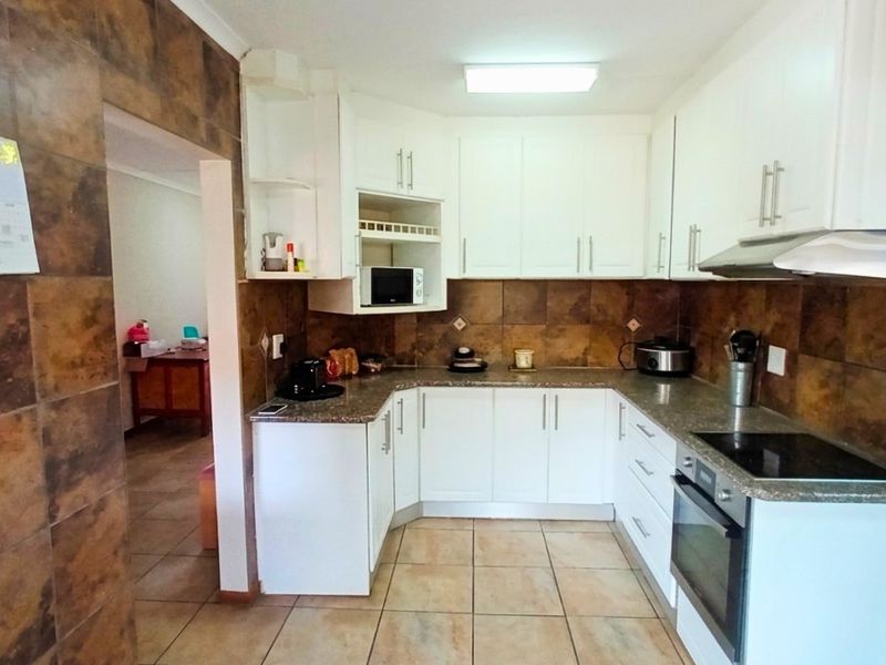 Functional kitchen featuring white cabinetry, granite-look countertops, built-in oven, electric hob, and extractor fan, complemented by tiled walls and flooring.