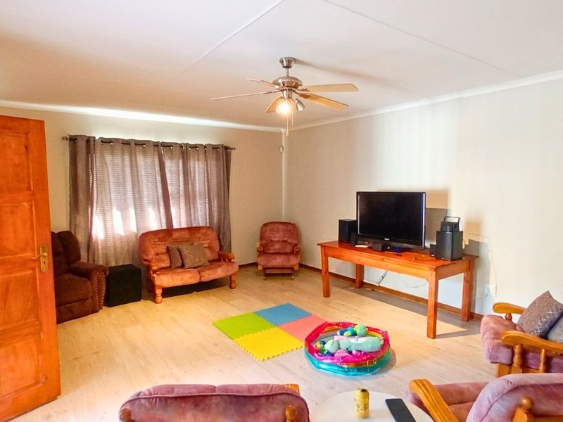 Spacious living room featuring light-toned laminate flooring, a ceiling fan, and a solid timber door.
