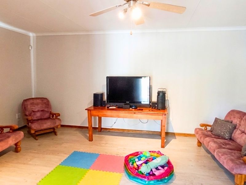 A spacious living room featuring light-toned flooring, a ceiling fan, and neutral wall finishes, providing a versatile area for relaxation and family activities.