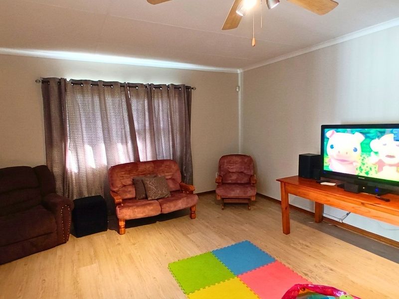 A living room featuring light-toned laminate flooring, a ceiling fan, and neutral wall finishes.