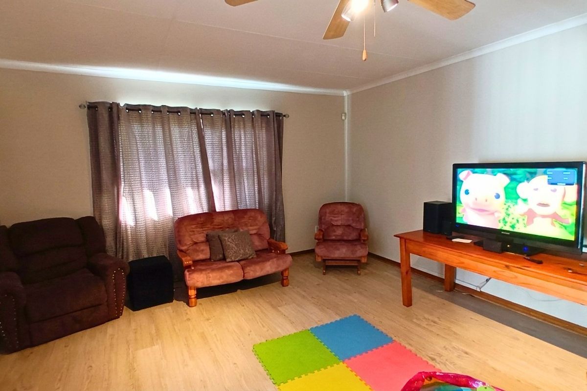 A living room featuring light-toned laminate flooring, a ceiling fan, and neutral wall finishes.