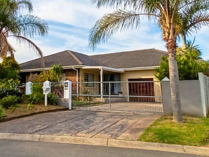 Front exterior view of a single-story house featuring a tiled roof, brick and plaster facade, secure gated entrance, and a paved driveway.