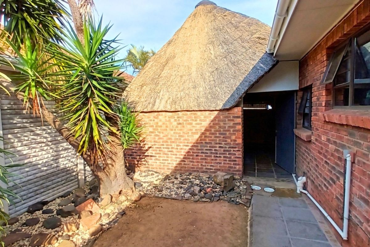 A rear exterior view of the property featuring a traditional thatched roof structure, brick facade, and a paved walkway leading to an entrance.