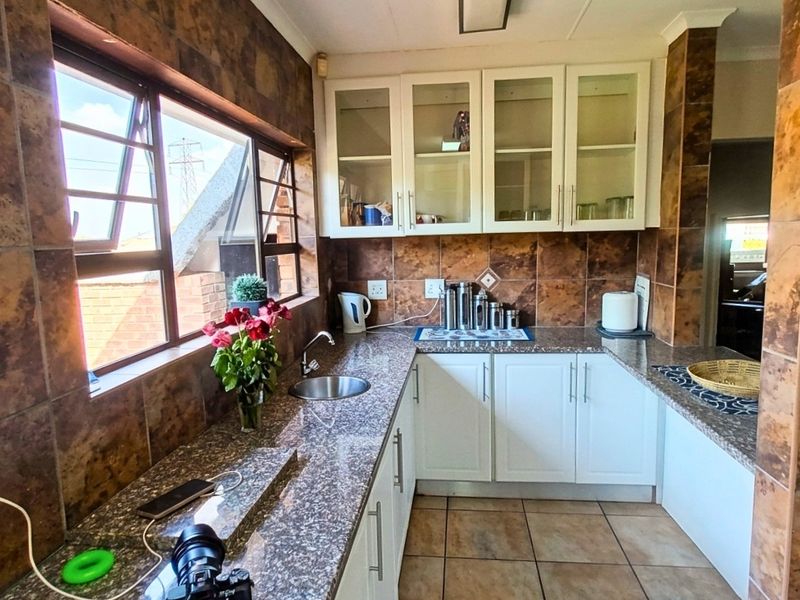 A functional kitchen featuring granite countertops, white cabinetry, glass-fronted upper cabinets, and tiled wall finishes.
