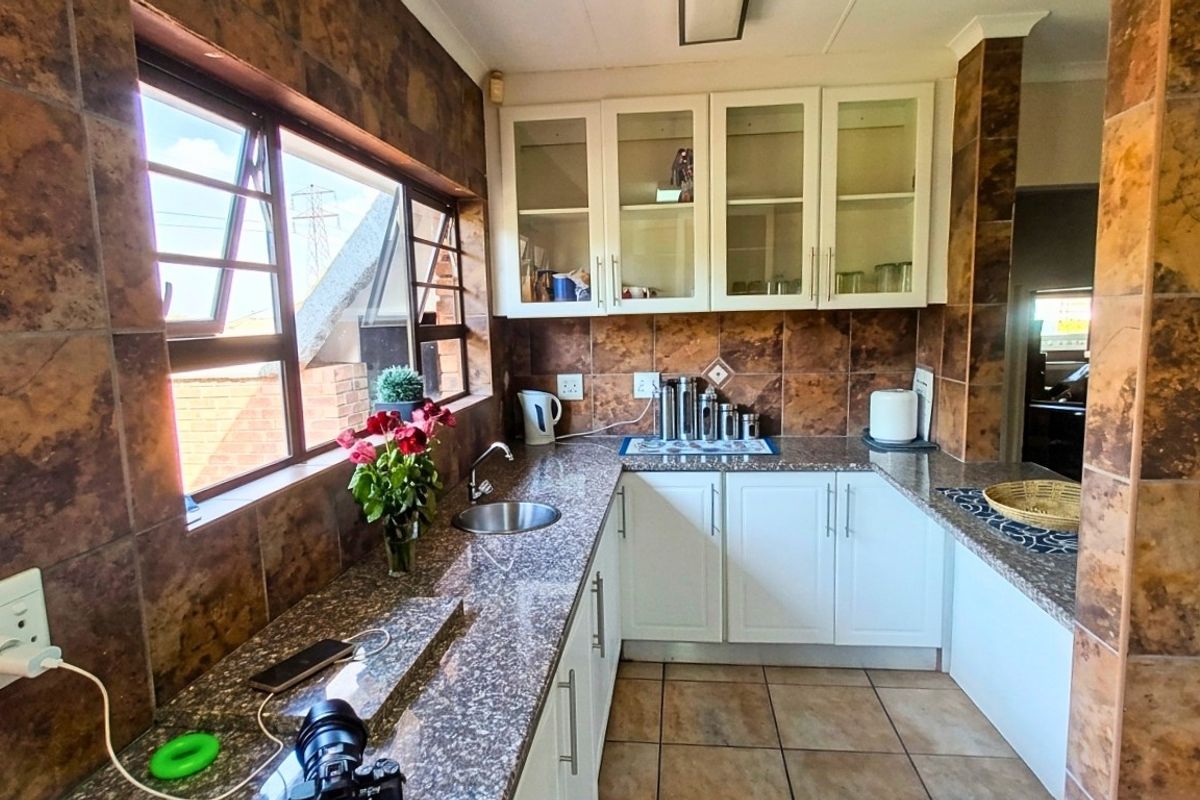 A functional kitchen featuring granite countertops, white cabinetry, glass-fronted upper cabinets, and tiled wall finishes.