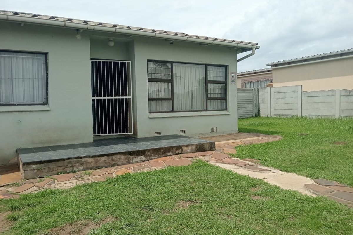 Rear view of the house featuring a tiled patio area, security gates on the entrance, and a spacious grass garden with perimeter walling.