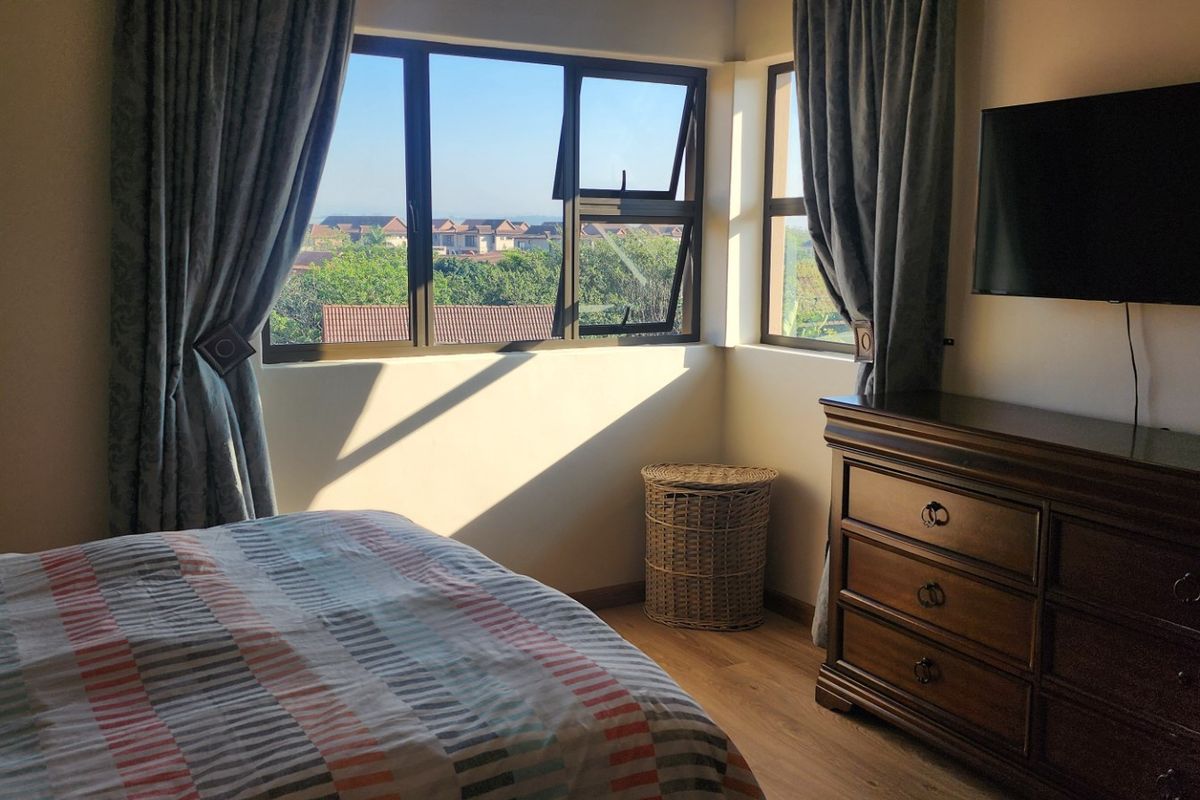 A well-lit bedroom featuring laminate flooring and large aluminium-framed windows offering an elevated view of the surrounding neighbourhood.