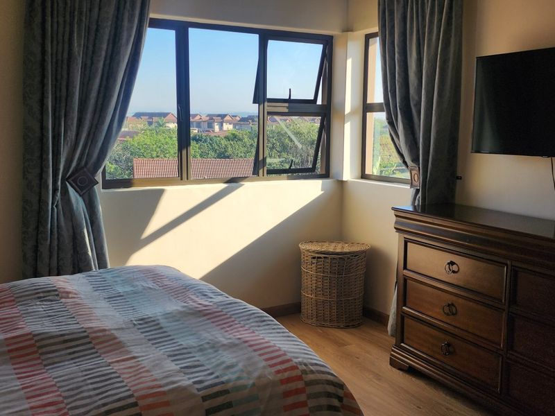 A well-lit bedroom featuring laminate flooring and large aluminium-framed windows offering an elevated view of the surrounding neighbourhood.