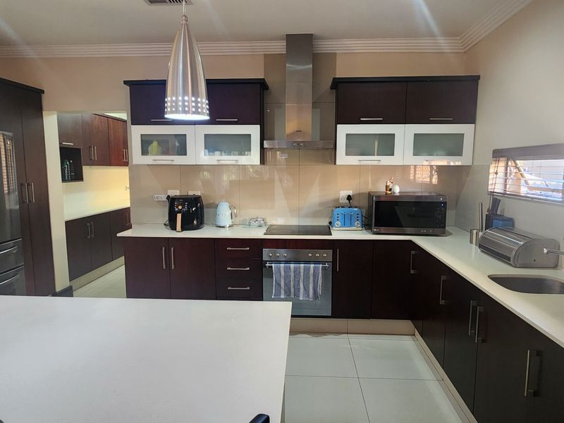 Modern kitchen featuring dark wood cabinetry, contrasting white upper cabinets, stone countertops, stainless steel appliances, and a central island with pendant lighting.
