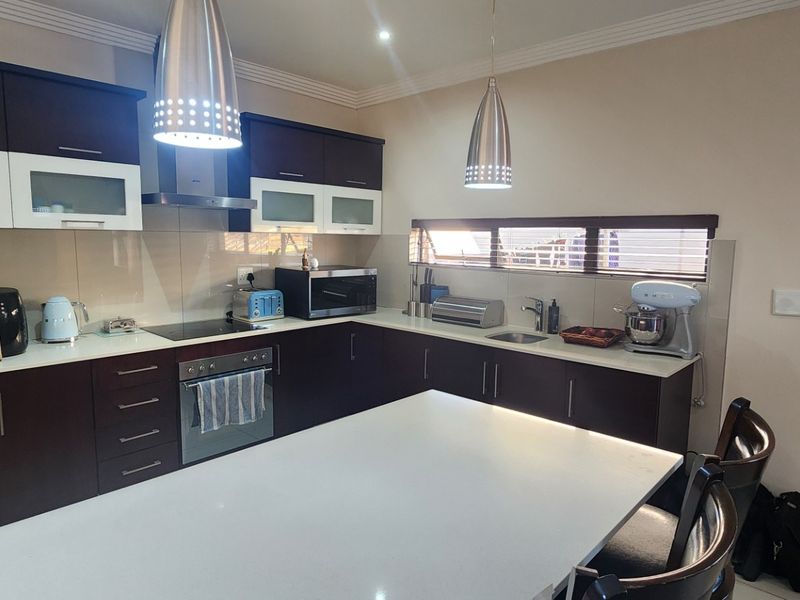Modern kitchen featuring dark wood cabinetry, contrasting white stone countertops, integrated appliances, and stylish pendant lighting over a central breakfast island.