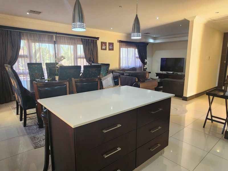 Spacious open-plan living and dining area featuring a central kitchen island, tiled flooring, and modern recessed lighting throughout the integrated space.