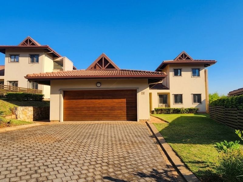 Front elevation of a townhouse featuring a paved driveway, double garage with timber door, and well-maintained garden surroundings.