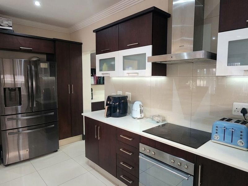 Modern kitchen featuring dark wood cabinetry, stone countertops, integrated stainless steel appliances, and a sleek glass splashback with recessed lighting.