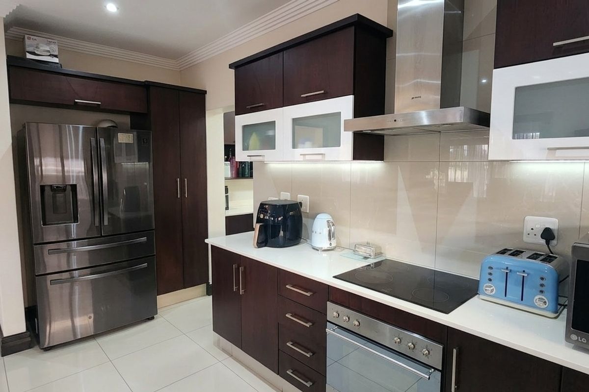 Modern kitchen featuring dark wood cabinetry, stone countertops, integrated stainless steel appliances, and a sleek glass splashback with recessed lighting.