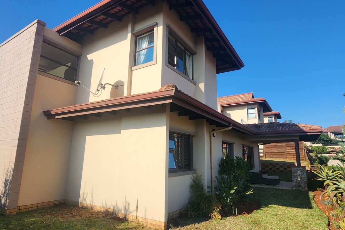 A view of the rear elevation of the townhouse, featuring a tiled roof, covered patio area, and established garden surroundings.
