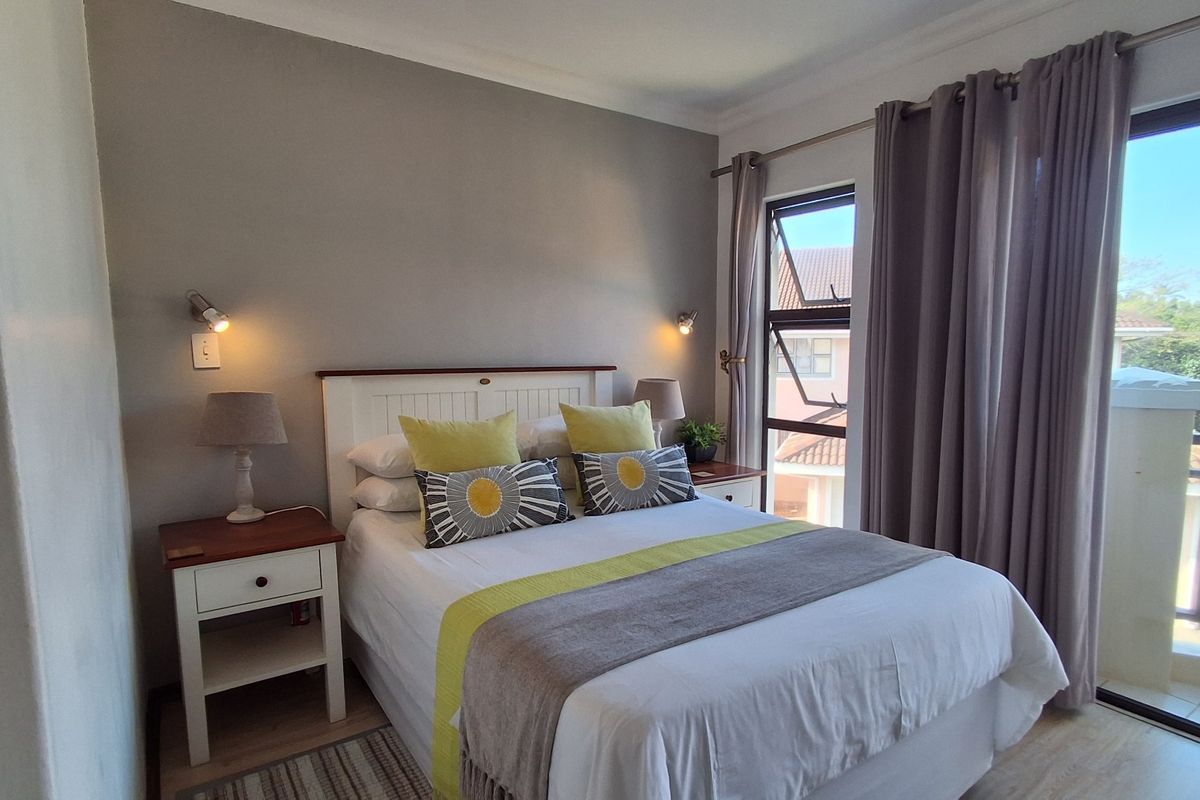 A well-lit bedroom featuring neutral wall tones, laminate flooring, and a large window with direct access to a private balcony.