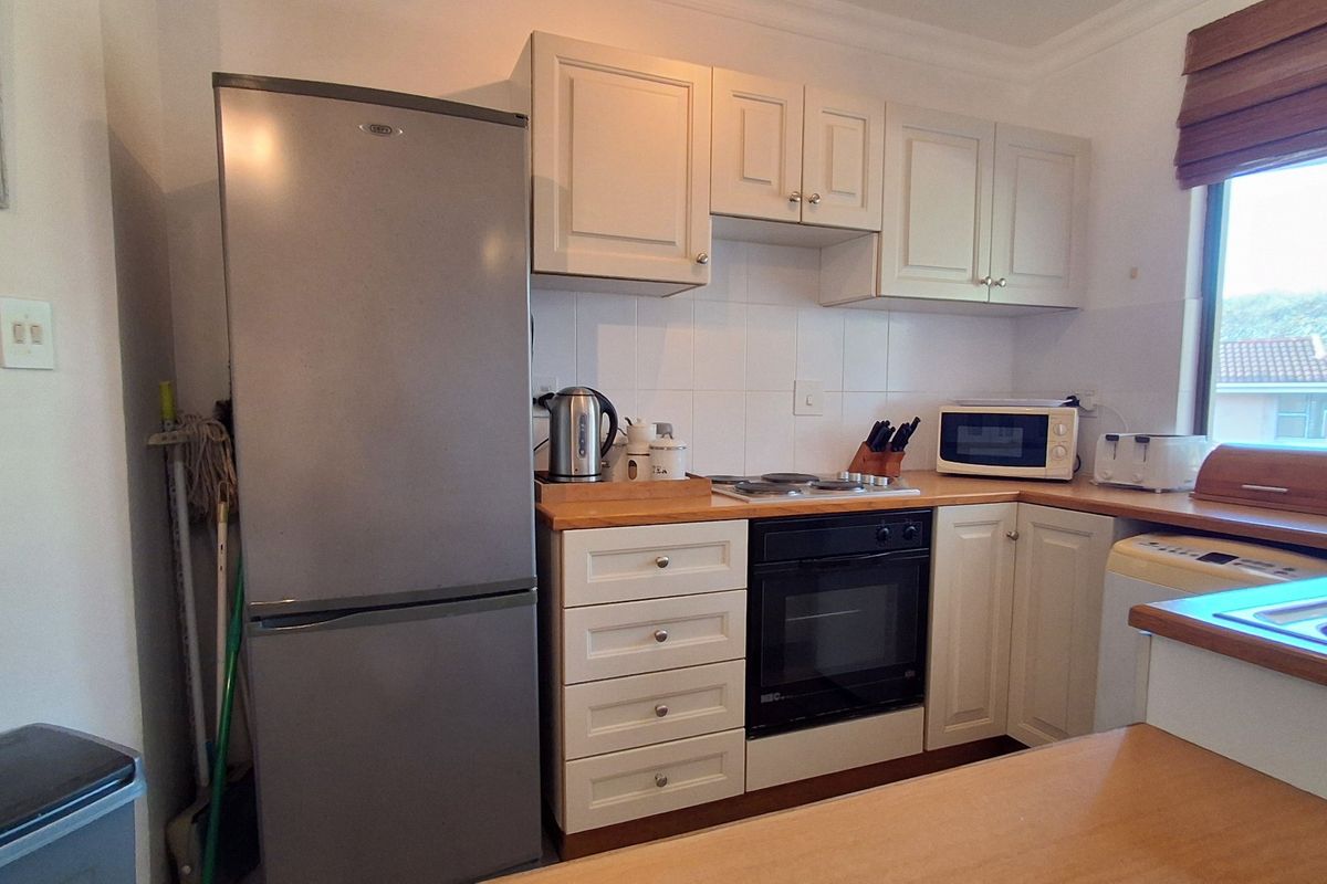 A compact kitchen featuring cream cabinetry, wooden countertops, a built-in oven, and a hob, with a window providing natural light.