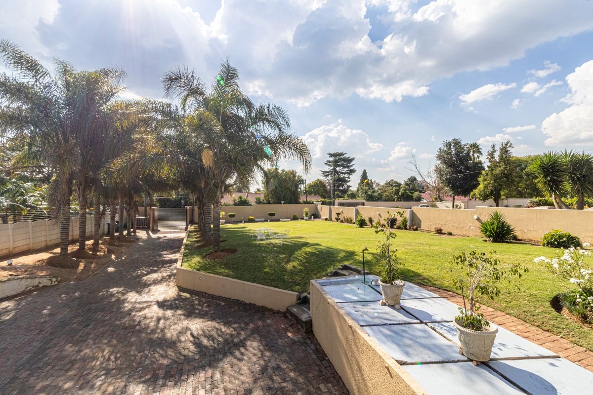 Spacious rear garden featuring a manicured lawn, established palm trees, and a paved driveway area enclosed by high boundary walls.