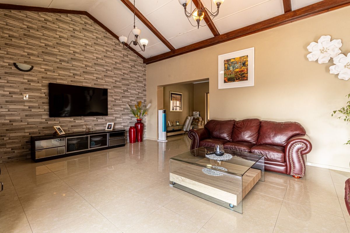 Spacious living room featuring a vaulted ceiling with exposed timber beams, tiled flooring, and a textured stone feature wall.