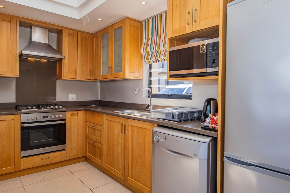 A functional kitchen featuring light wood cabinetry, stone-look countertops, a stainless steel oven, extractor fan, and integrated sink area.