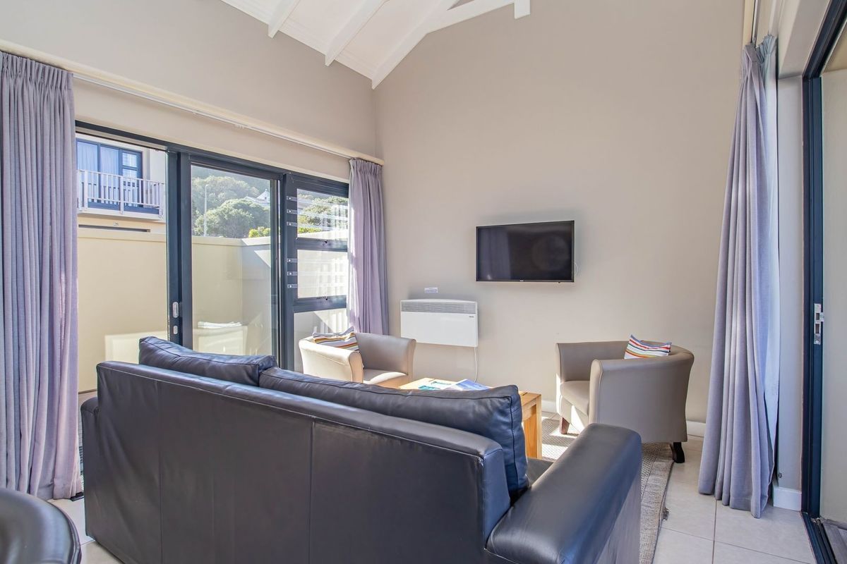 A bright living room featuring high vaulted ceilings, tiled flooring, and large sliding glass doors that open onto an outdoor patio area.