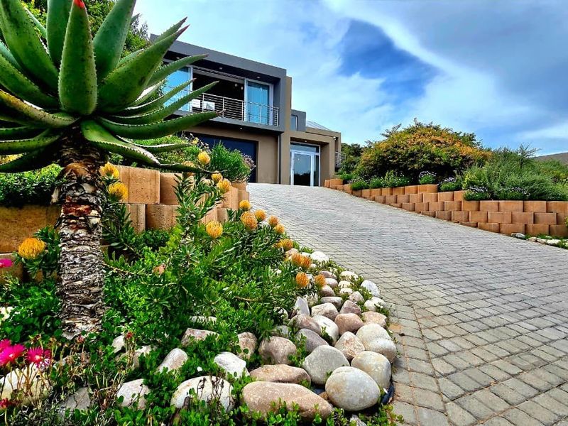 Modern multi-level residence featuring a paved driveway, landscaped retaining walls, and an upper-level balcony with sliding glass doors.
