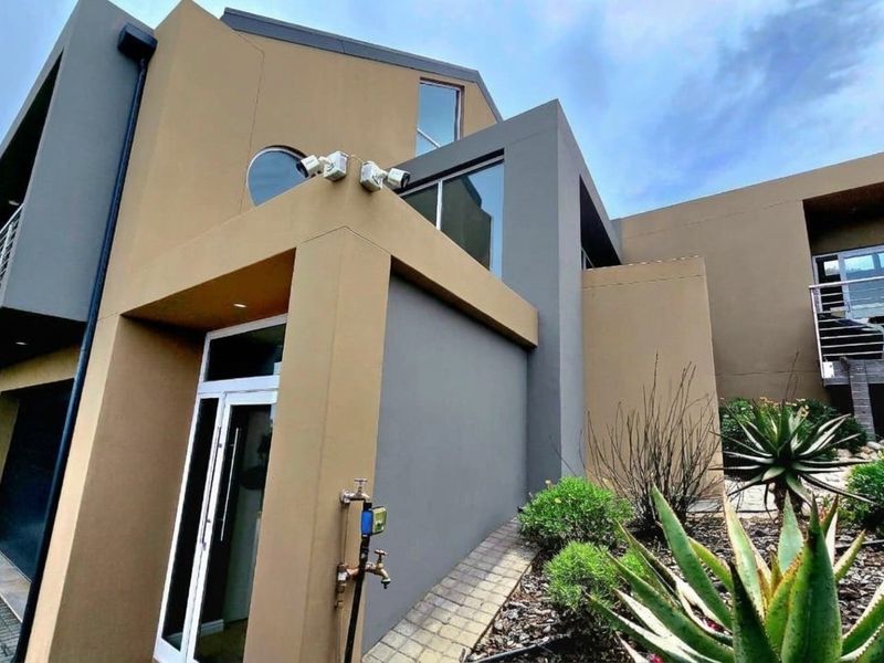 Modern multi-level residential exterior featuring contemporary architectural design, paved driveway, integrated garage, and balcony with metal railing.