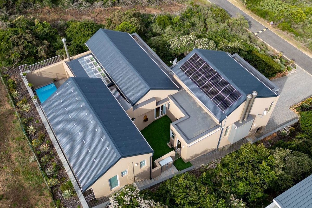 Aerial view of a modern residential property featuring a metal roof with integrated solar panels, a private courtyard, and a swimming pool.