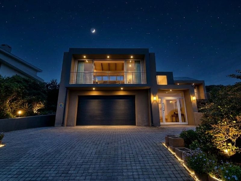 Modern double-story residence featuring a paved driveway, automated garage, and an upper-level balcony, beautifully illuminated for evening appeal.