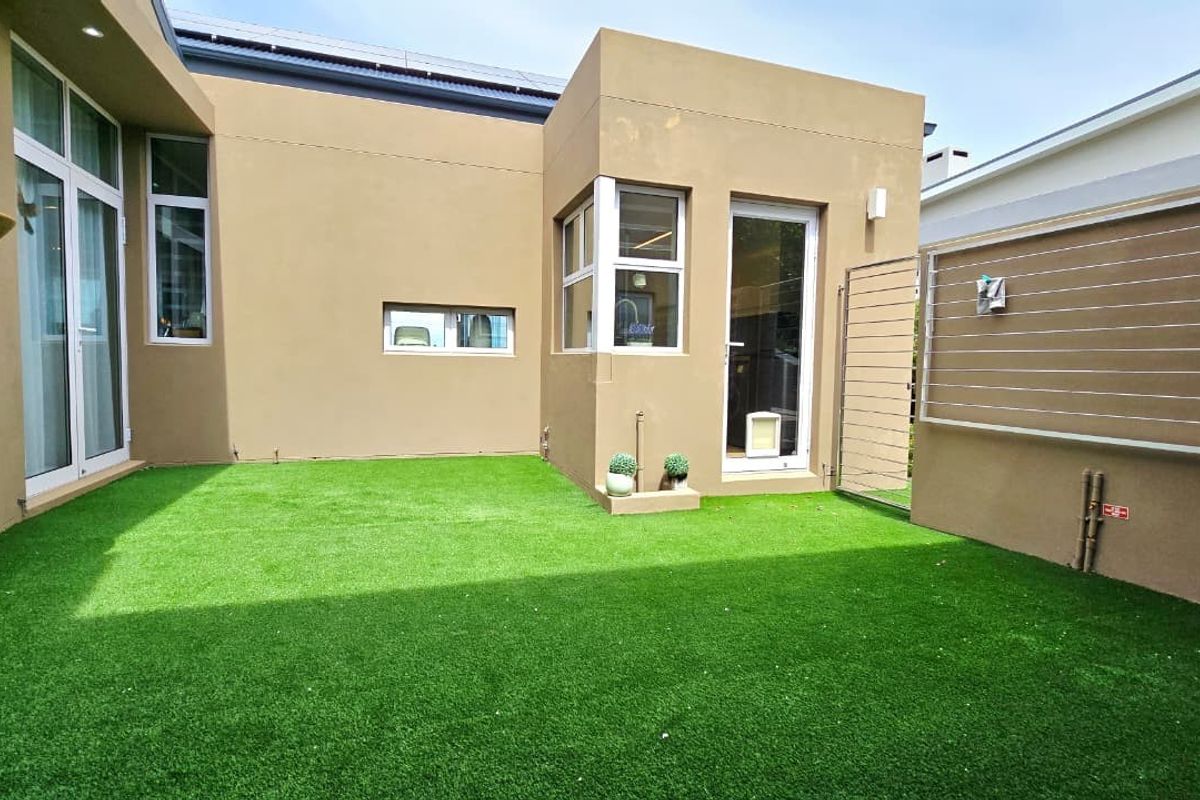 A well-maintained rear courtyard featuring artificial turf, modern sliding glass doors, and secure perimeter fencing.