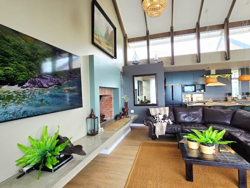 Spacious open-plan living area featuring a vaulted ceiling with exposed beams, a brick fireplace with concrete hearth, and a modern integrated kitchen.
