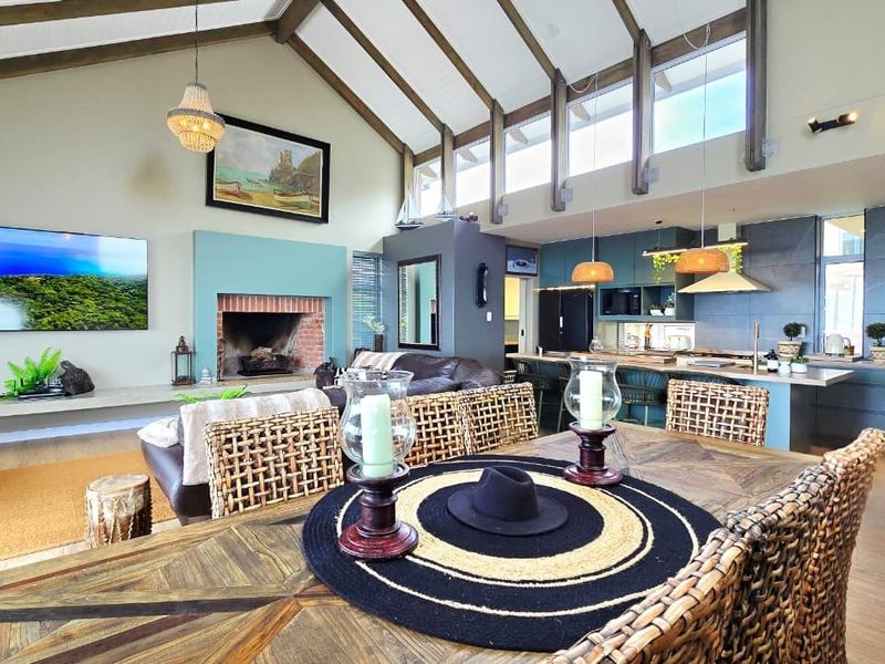 Spacious open-plan living area featuring a vaulted ceiling with exposed beams, a brick fireplace, and a modern kitchen with a central island.