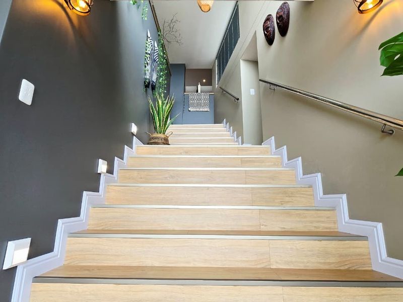 A well-lit interior staircase featuring modern laminate treads, a stainless steel handrail, and integrated wall-mounted accent lighting.