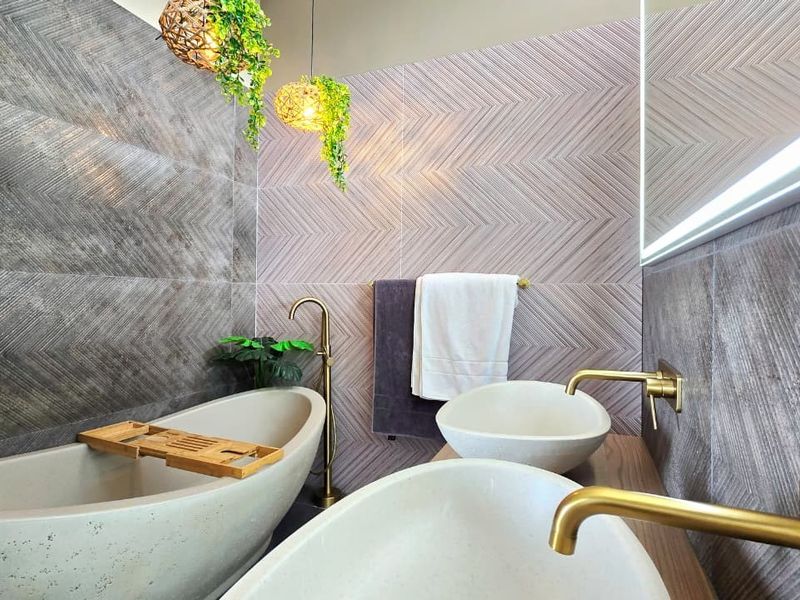 Modern luxury bathroom featuring a freestanding bathtub, dual vessel sinks with brass fixtures, and stylish chevron-patterned wall tiling.