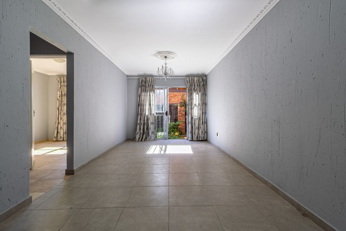 An empty living room featuring tiled flooring, textured walls, decorative ceiling cornices, and a sliding glass door leading to an outdoor area.