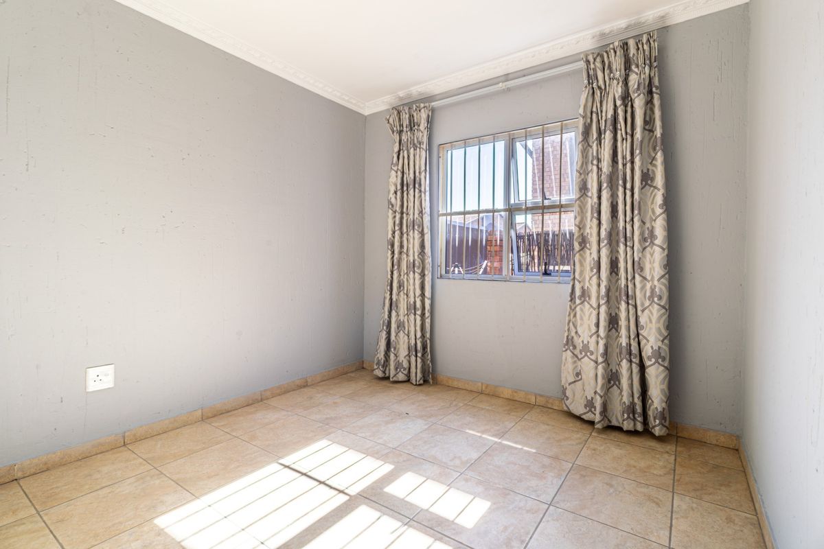 A vacant bedroom featuring neutral grey walls, tiled flooring, and a window fitted with security bars.