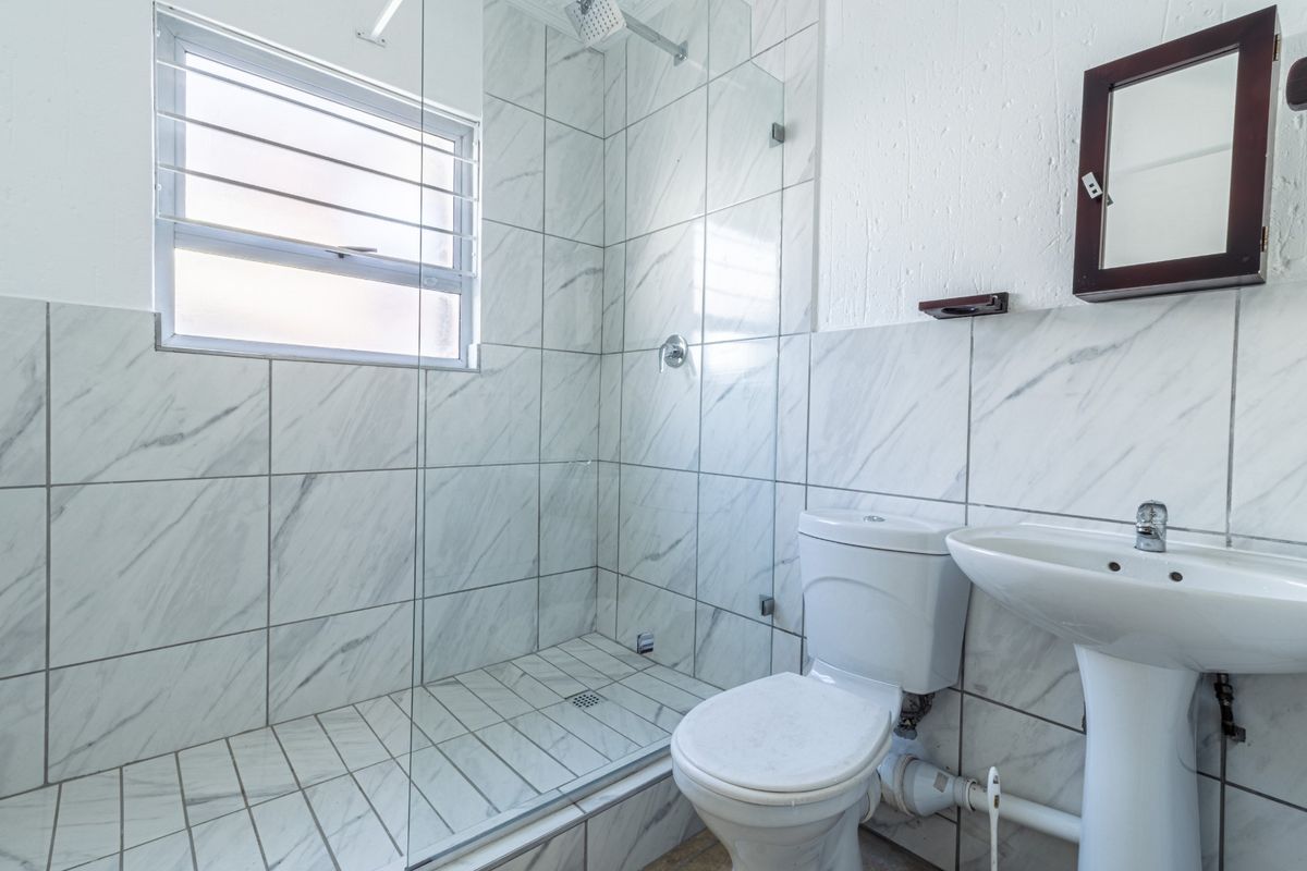 A functional bathroom featuring a walk-in shower with glass enclosure, marble-look wall tiles, a pedestal basin, and a standard toilet.