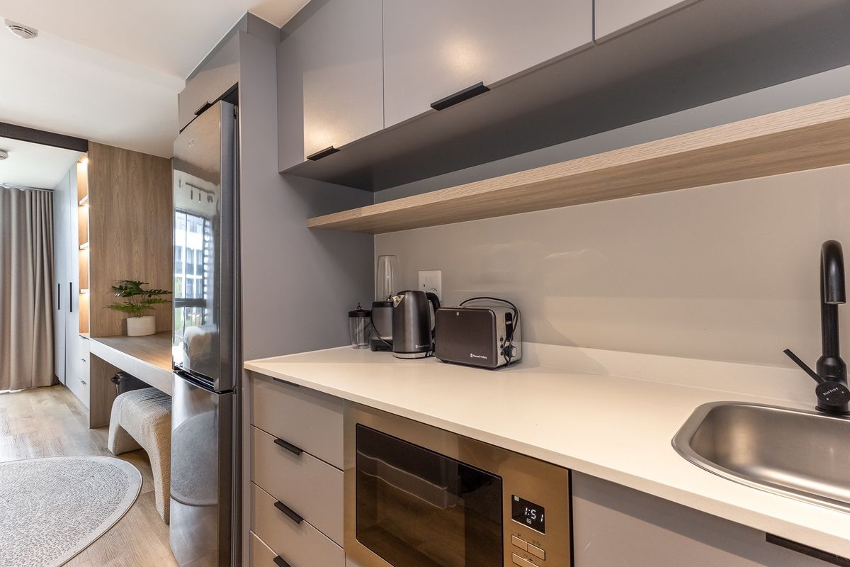 Modern compact kitchen featuring sleek grey cabinetry, stone countertops, integrated appliances, and a minimalist sink with a black mixer tap.