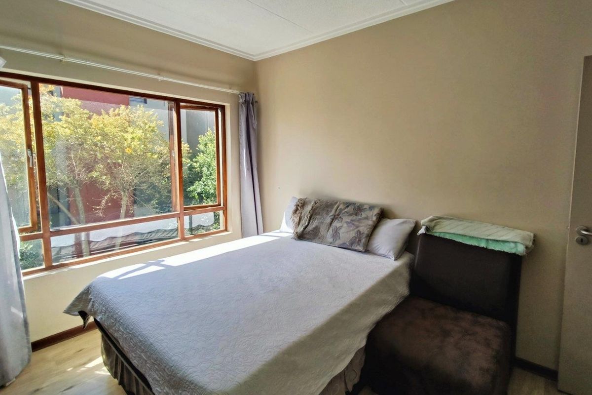 A bedroom featuring large wooden-framed windows, light-toned laminate flooring, and neutral wall finishes.