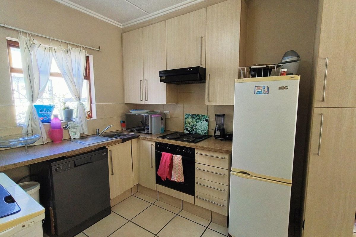 Compact kitchen featuring light wood-finish cabinetry, tiled flooring, built-in oven, hob, and extractor fan with integrated sink and dishwasher space.