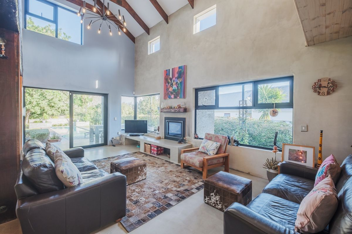 Spacious living room featuring a high vaulted ceiling with exposed timber beams, concrete floors, a built-in fireplace, and large windows overlooking the pool area.