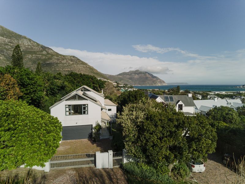 Aerial view of a modern residential property featuring a paved driveway, garage, and solar panels, set against a scenic mountain and coastal backdrop.
