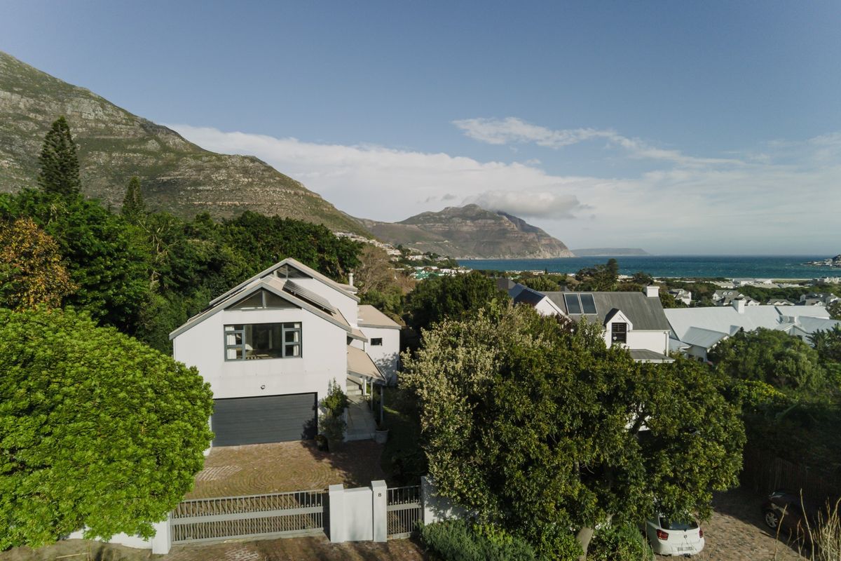 Aerial view of a modern residential property featuring a paved driveway, garage, and solar panels, set against a scenic mountain and coastal backdrop.