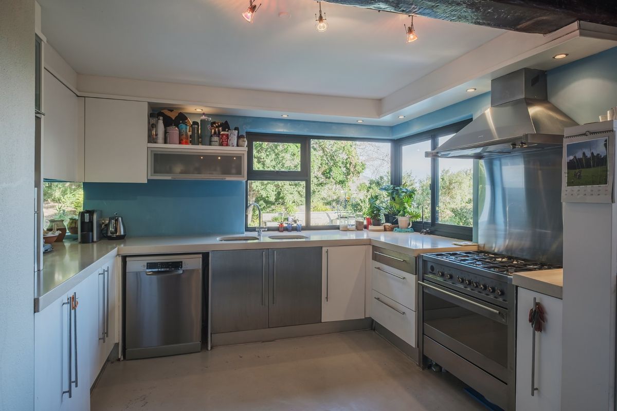 A functional kitchen featuring stainless steel appliances, stone countertops, ample cabinetry, and a corner window providing natural light and garden views.