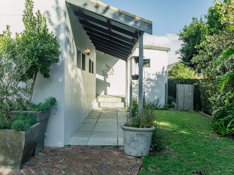 A well-maintained rear exterior featuring a covered walkway with a timber pergola, stone paving, and a landscaped garden area with a timber gate.