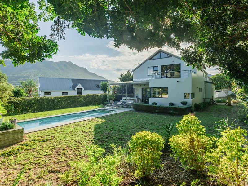 Rear view of a multi-story house featuring a swimming pool, landscaped garden, and an upper-level balcony with mountain views.