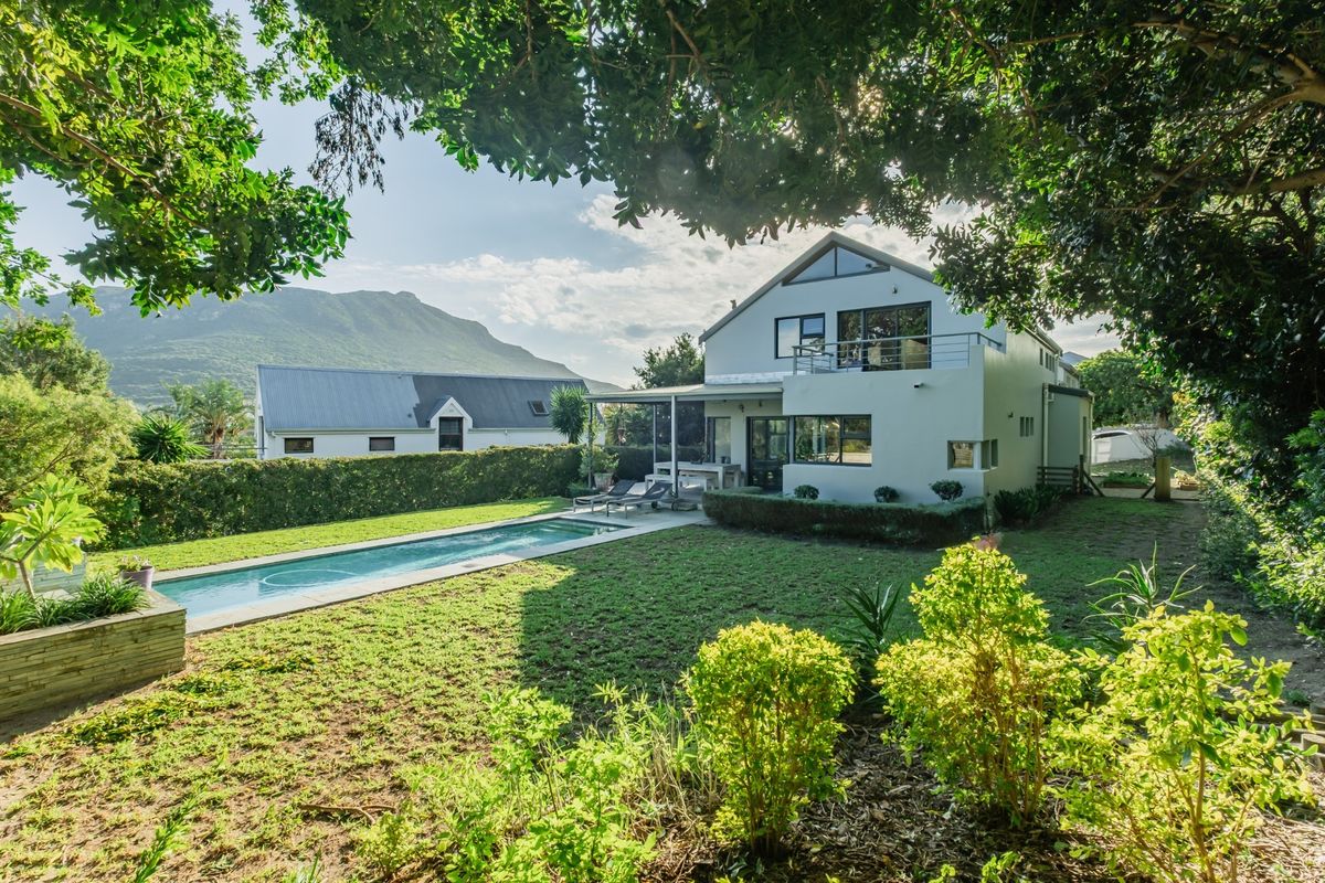 Rear view of a multi-story house featuring a swimming pool, landscaped garden, and an upper-level balcony with mountain views.
